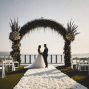 A bride and groom share a joyful moment under a floral arch during an outdoor wedding ceremony.