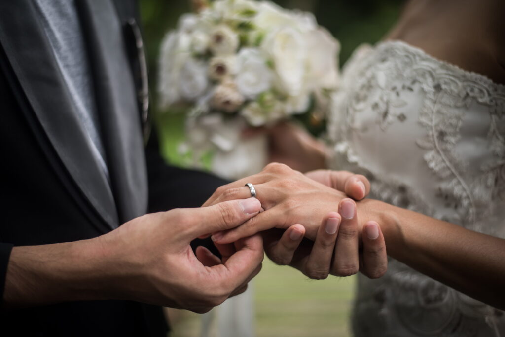 Close-up of a groom's hands placing a wedding ring on the bride's finger during their ceremony.