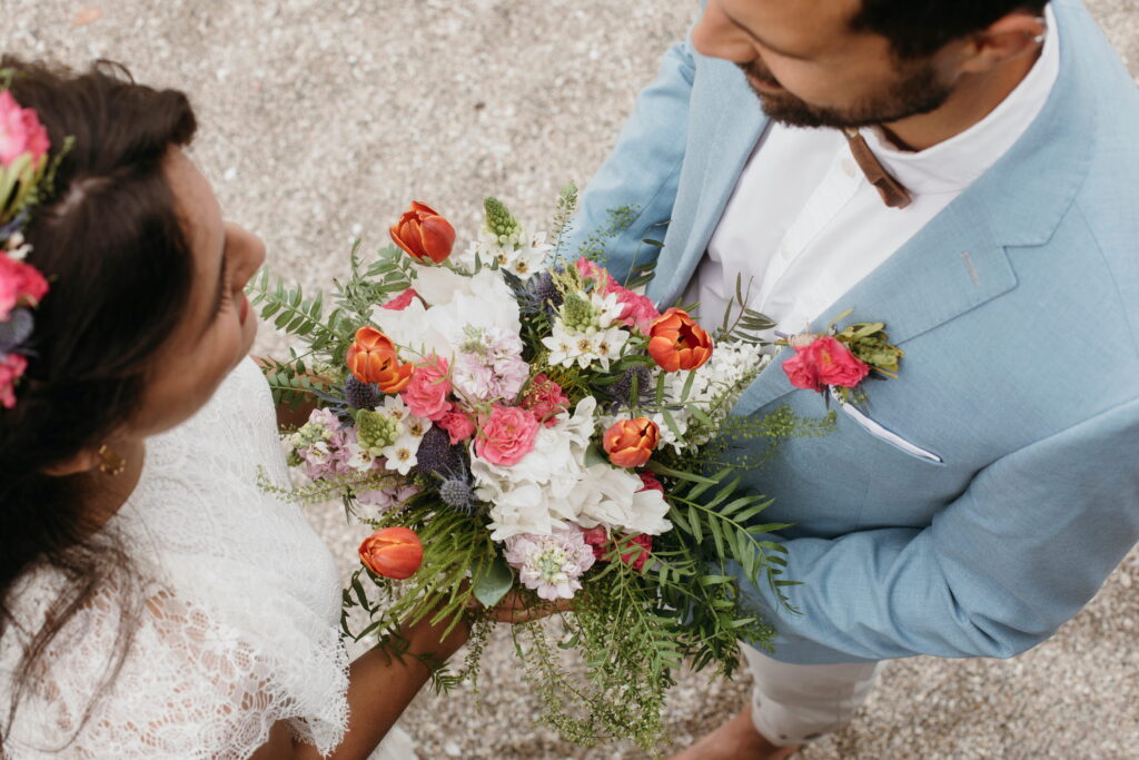 A bride and groom embrace and laugh on a sandy beach with turquoise ocean waves in the background