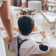 A boy in suspenders reaching for food at a wedding reception buffet table
