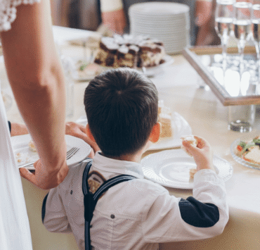A boy in suspenders reaching for food at a wedding reception buffet table