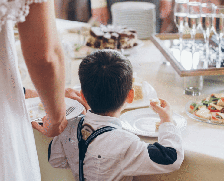 A boy in suspenders reaching for food at a wedding reception buffet table