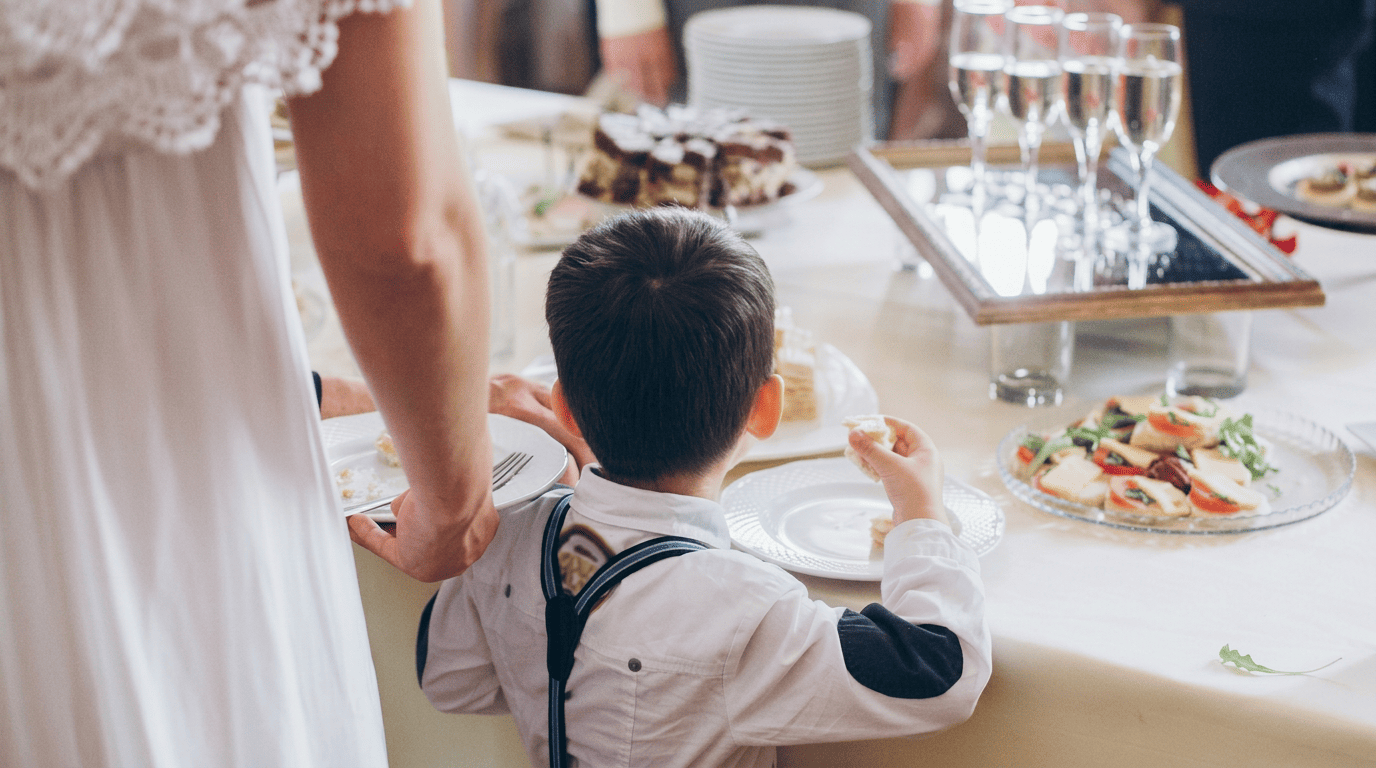 A boy in suspenders reaching for food at a wedding reception buffet table