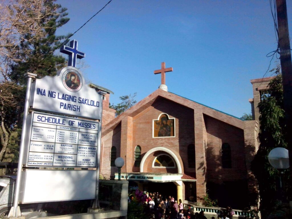 A modern church facade with a large white cross and a distinct curved roof design against a blue sky.