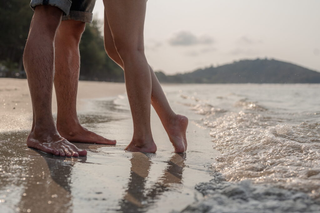 A man’s and a woman’s feet by the water.