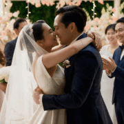 Couple exchanging their first kiss as newlyweds surrounded by bridesmaids and groomsmen at a floral garden wedding