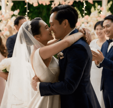 Couple exchanging their first kiss as newlyweds surrounded by bridesmaids and groomsmen at a floral garden wedding